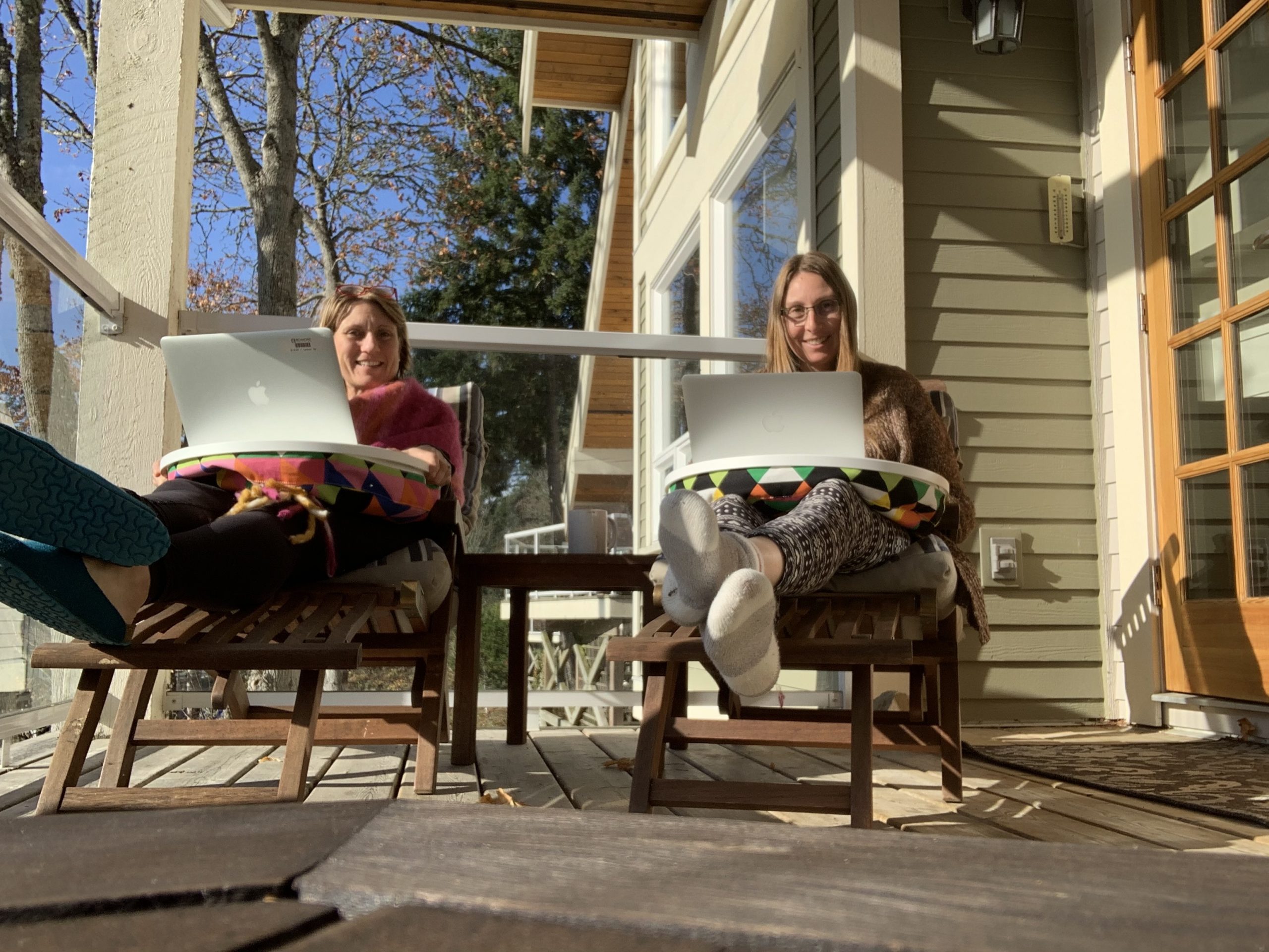 Elspeth and Rowena sitting in lounge chairs on the deck, both typing on laptops