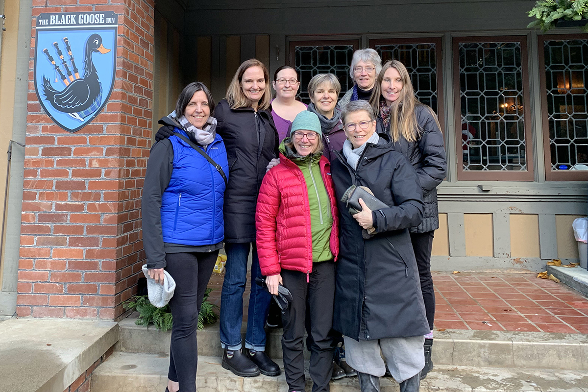 The eight partners of West Coast Editorial Associates standing outside the Black Goose Inn in Parksville, British Columbia, wearing winter jackets, scarves, and toques.