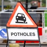 A Road Sign Warns Drivers Of Pothole Hazards Ahead.