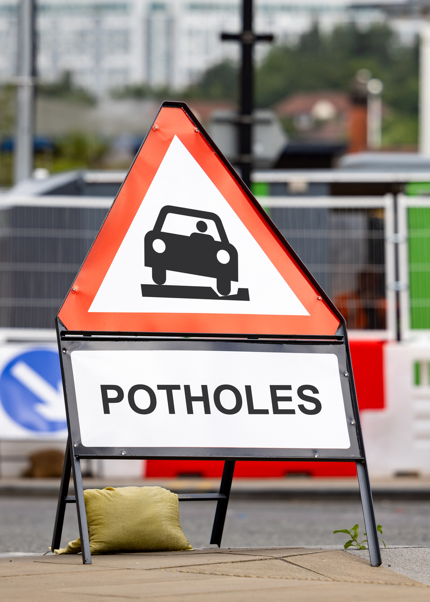 A road sign warns drivers of pothole hazards ahead.