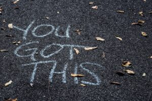 The words "You Got This" written in chalk on the ground, with a few fallen leaves strewn around