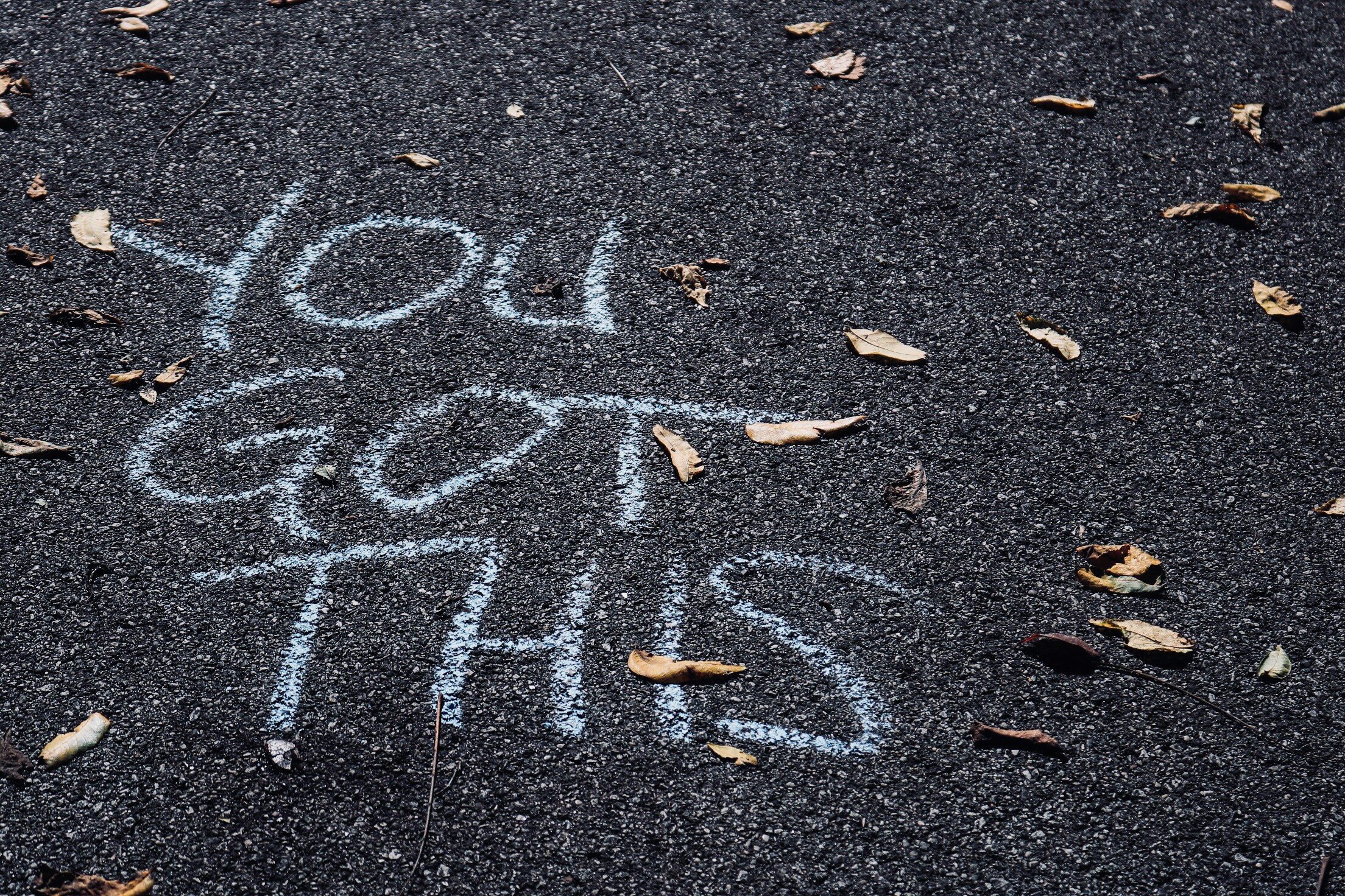 The words "You Got This" written in chalk on the ground, with a few fallen leaves strewn around