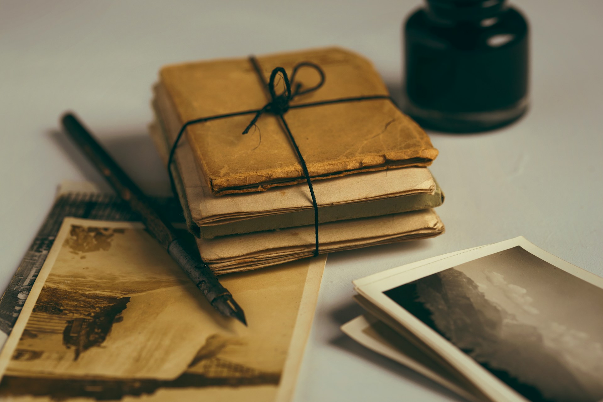 A stack of yellowed old letters or papers tied with a string, with a few old photos, fountain pen, and inkwell lying on a table.