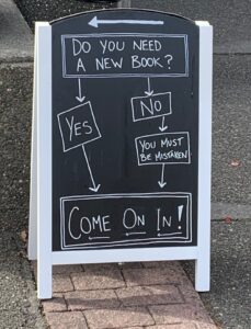 A sandwich board with a decision tree. The question "Do you need a new book?" leads to Yes and No answers. If Yes, the tree leads to "Come on in!" If No, the tree leads first to "You must be mistaken" and then to "Come on in!"